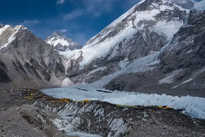 Bright yellow and orange mountaineering tents pitched directly on the rocky debris and ice pinnacles of Khumbu Glacier at Everest Base Camp