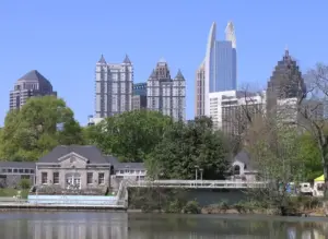 High-rise towers of the Midtown Atlanta skyline reflected across the surface of Clara Meer lake in Piedmont Park under a humid summer sky.
