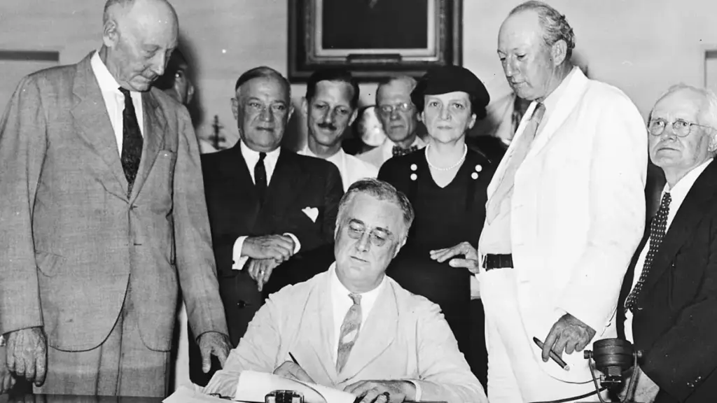 President Franklin D. Roosevelt signs the Social Security Act with officials gathered around a desk.
