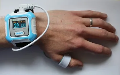 A wrist-worn smart monitoring device on a person’s arm with a small digital display.