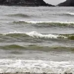 Breaking Pacific Ocean waves along a shoreline under grey sky and rough surf.