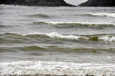 Breaking Pacific Ocean waves along a shoreline under grey sky and rough surf.