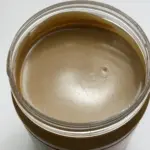 An open jar filled with smooth creamy peanut butter resting on a kitchen granite countertop.