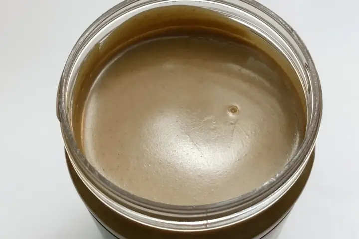 An open jar filled with smooth creamy peanut butter resting on a kitchen granite countertop.