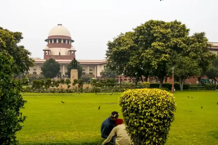 Exterior facade and central wing of the Supreme Court of India in New Delhi viewed across the institutional grounds and landscaped gardens.