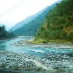 Teesta River flowing through a steep Himalayan valley with forested slopes and rocky riverbanks in Sikkim.