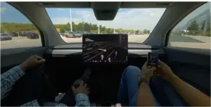 Interior view of a Tesla Cybercab showing the central screen and two passengers, with no steering wheel or foot pedals visible.