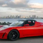 An electric sports car displayed outdoors on open pavement under direct daylight.