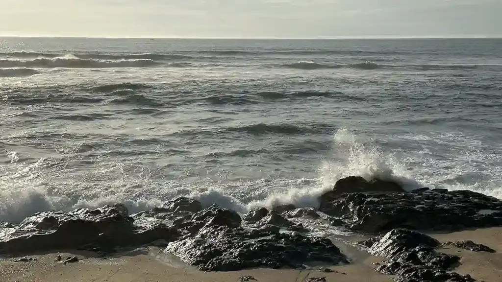 Rolling Atlantic ocean waves and white water surf breaking along an open shoreline under overcast skies.