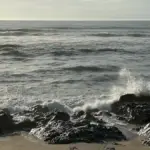 Rolling Atlantic ocean waves and white water surf breaking along an open shoreline under overcast skies.