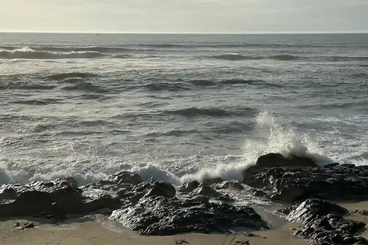 Rolling Atlantic ocean waves and white water surf breaking along an open shoreline under overcast skies.