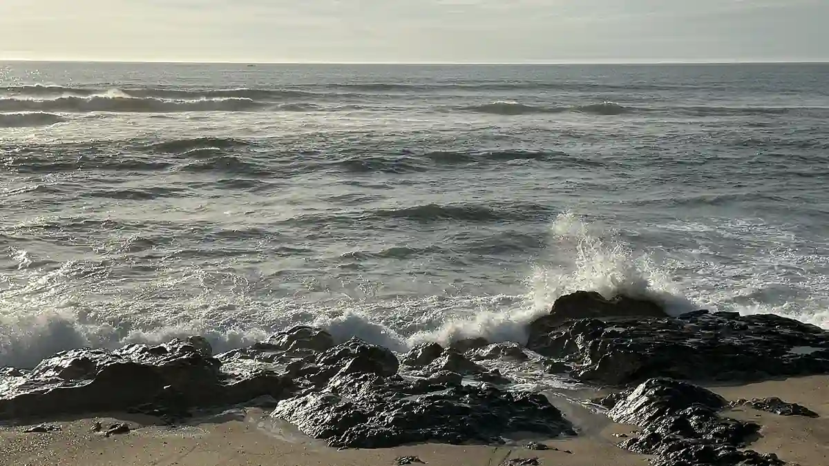 Rolling Atlantic ocean waves and white water surf breaking along an open shoreline under overcast skies.