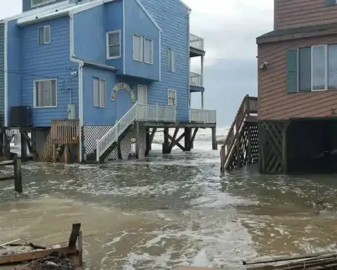 Floodwater surrounding raised homes after a coastal storm, used as a representative image for UK flood-risk coverage.