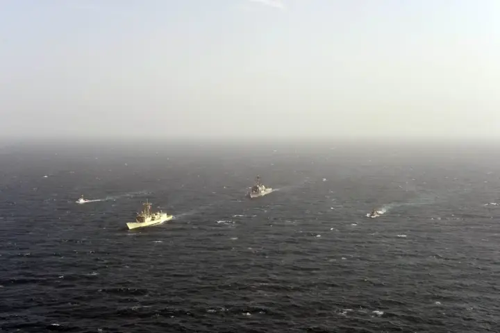 A gray naval guided-missile destroyer slicing through open ocean waters in the Persian Gulf during maritime security patrols.