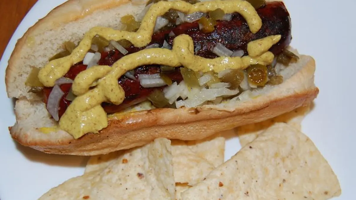 Prepared hot dog with mustard, diced onion, jalapeño and relish on a white plate.