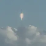 Falcon 9 rocket ascending from a launch pad with a bright plume against a dark sky.