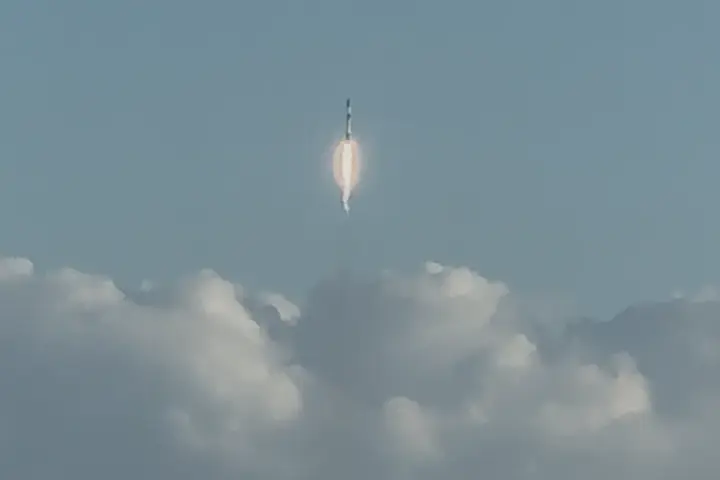 Falcon 9 rocket ascending from a launch pad with a bright plume against a dark sky.
