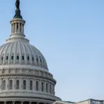 Close view of the white U.S. Capitol dome against a blue sky.