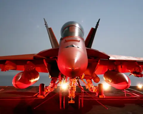 Photograph of a naval F/A-18 Super Hornet combat aircraft chained securely to the flight deck of a deployed U.S. Navy aircraft carrier at sea.