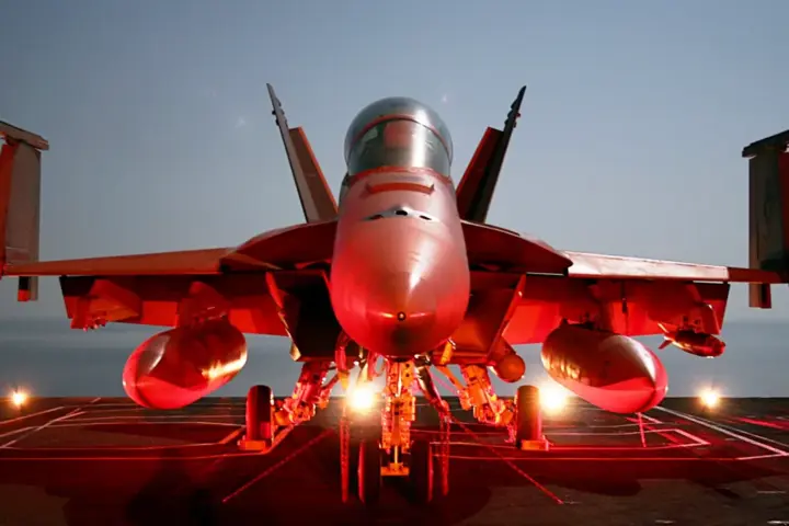 Photograph of a naval F/A-18 Super Hornet combat aircraft chained securely to the flight deck of a deployed U.S. Navy aircraft carrier at sea.