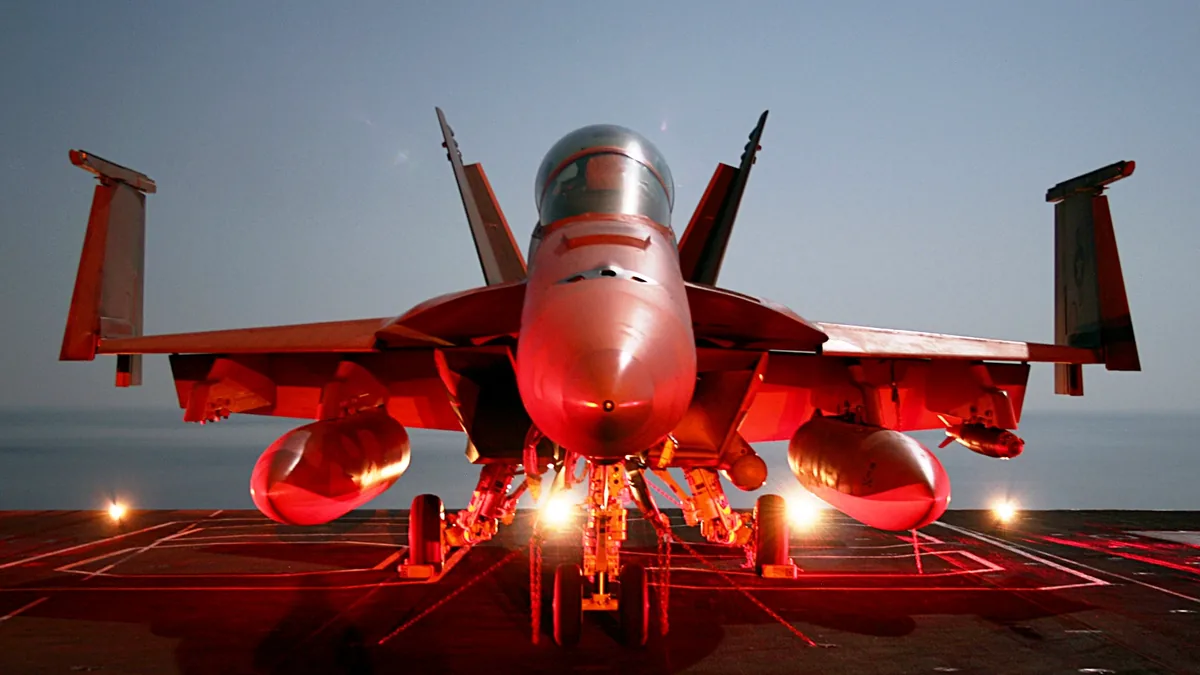 Photograph of a naval F/A-18 Super Hornet combat aircraft chained securely to the flight deck of a deployed U.S. Navy aircraft carrier at sea.