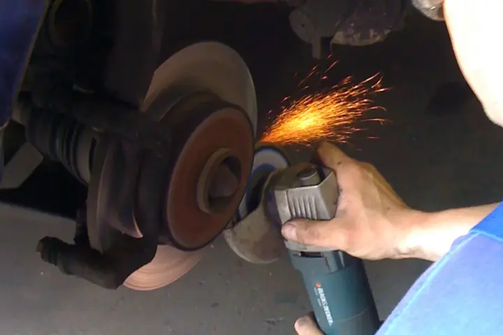 A mechanic working on an automotive brake disc with a handheld grinder.