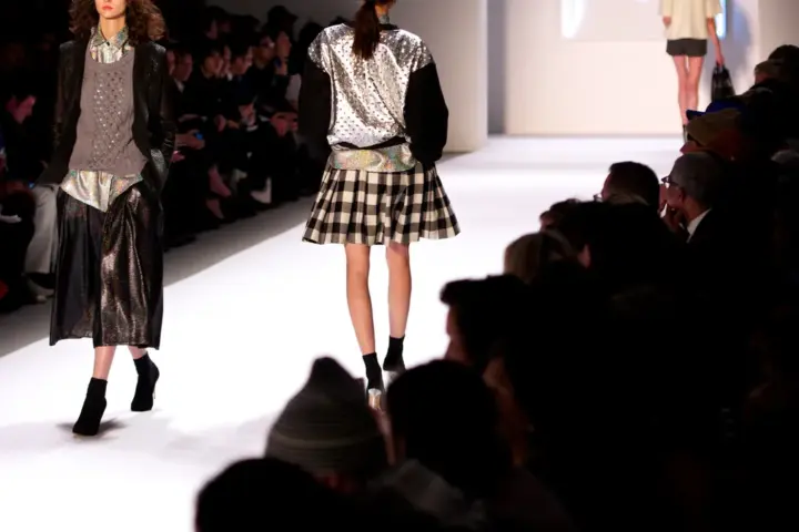 Models walking a fashion runway under stage lighting.