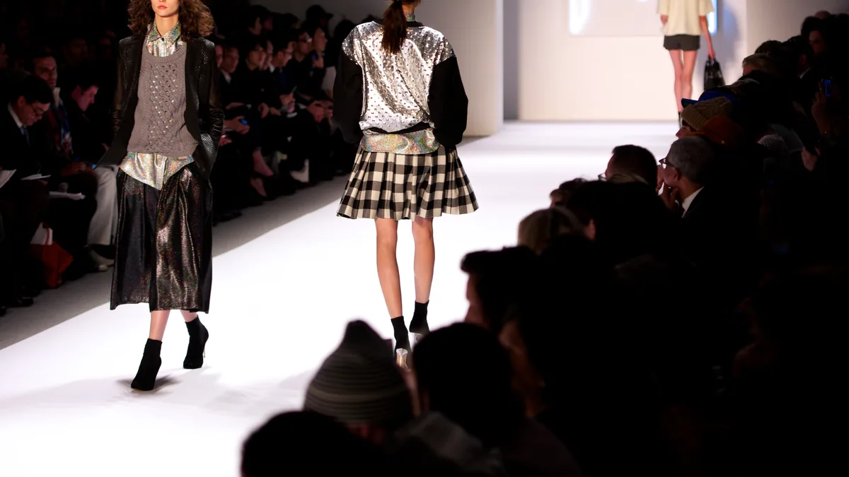 Models walking a fashion runway under stage lighting.