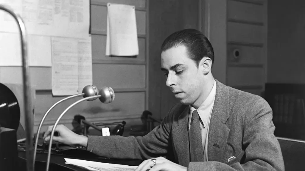 A radio announcer works beside microphones in a studio.