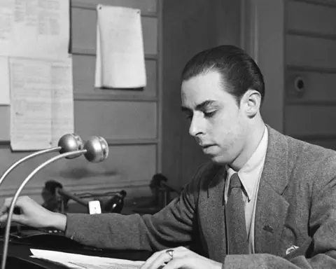A radio announcer works beside microphones in a studio.