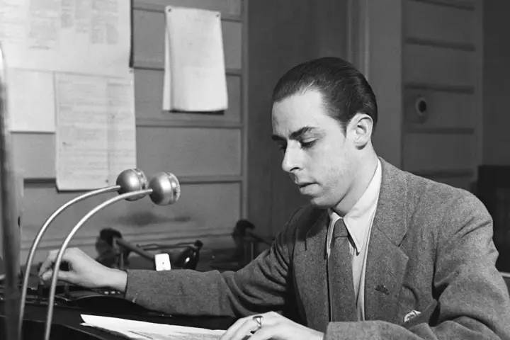 A radio announcer works beside microphones in a studio.
