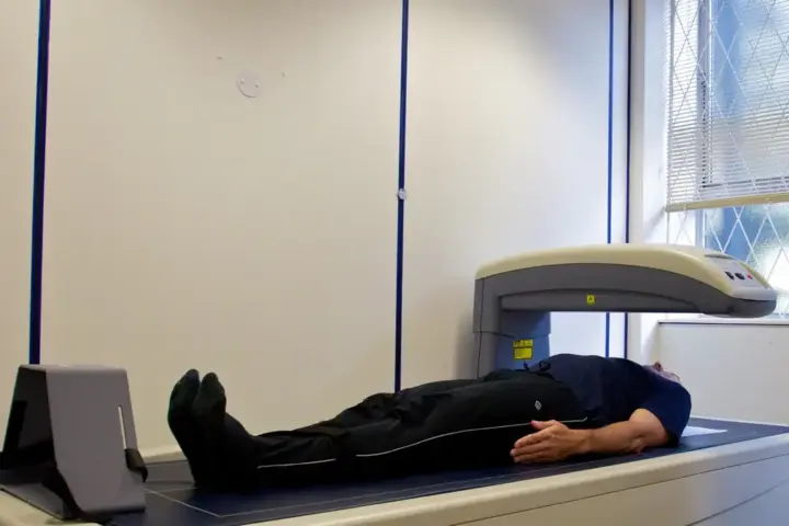 Person undergoing a DEXA body-composition scan in a clinical room, illustrating assessment of body fat distribution.