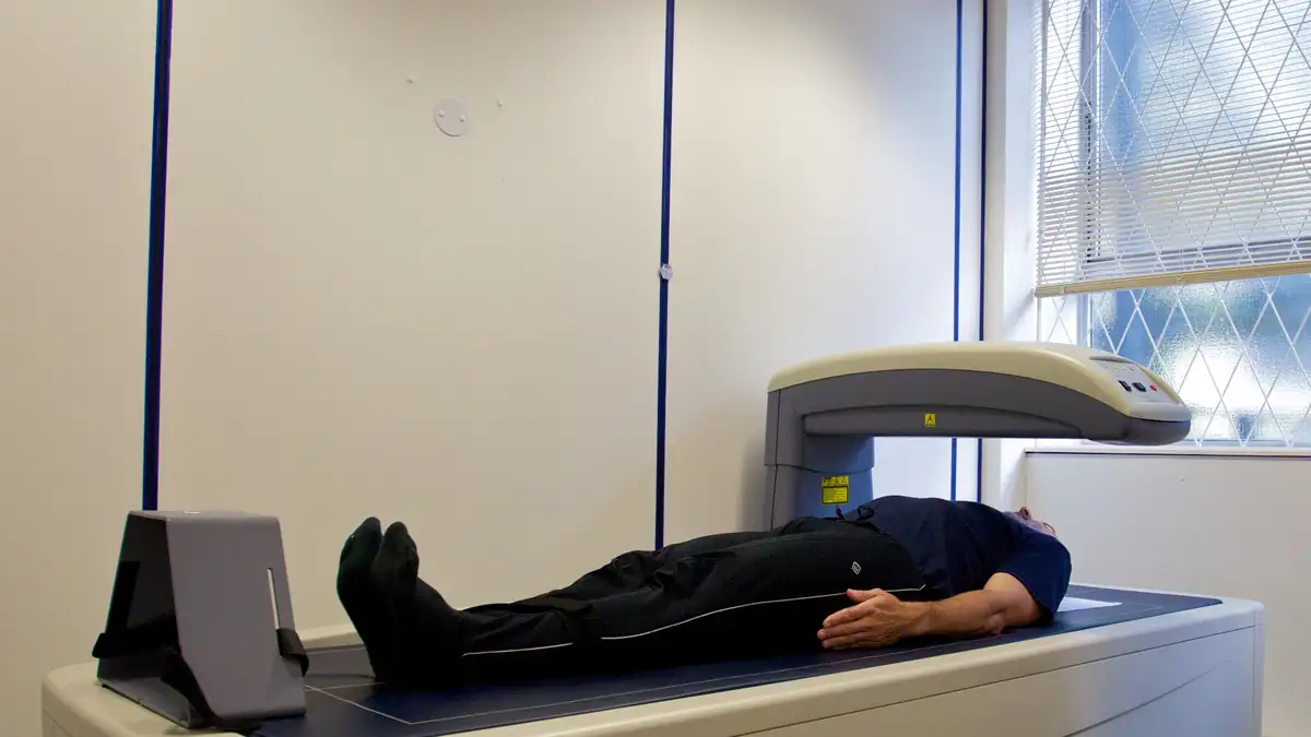 Person undergoing a DEXA body-composition scan in a clinical room, illustrating assessment of body fat distribution.