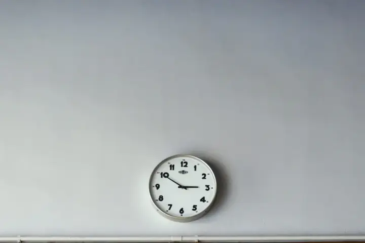 Close-up of a round analog wall clock face with black numerals and hands on a plain background