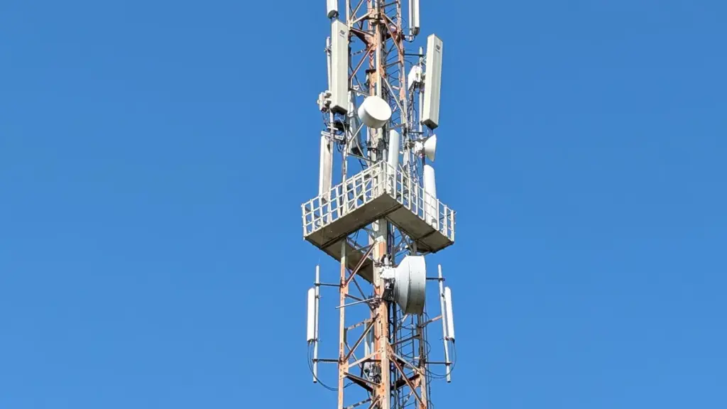 A mobile telecommunications tower with multiple antennas against a clear blue sky in India