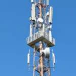 A mobile telecommunications tower with multiple antennas against a clear blue sky in India
