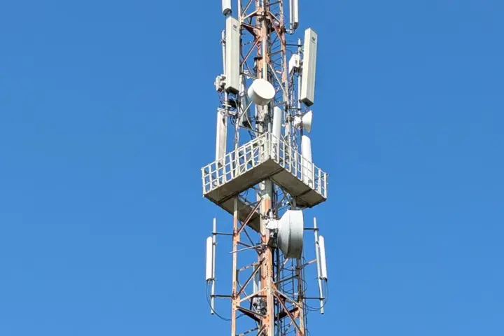 A mobile telecommunications tower with multiple antennas against a clear blue sky in India
