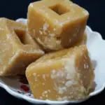 Unrefined golden-brown jaggery gur cubes served on a decorative plate