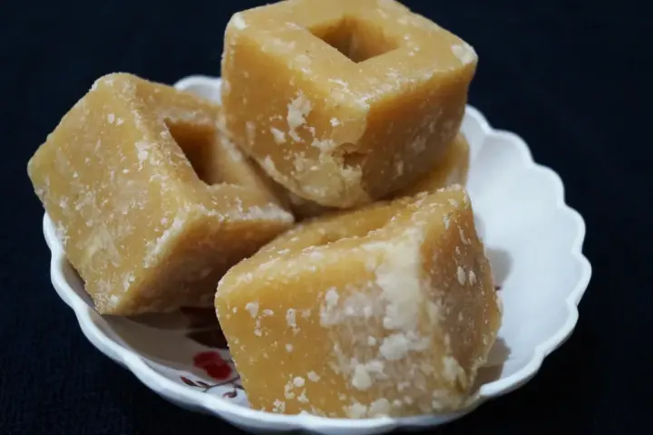 Unrefined golden-brown jaggery gur cubes served on a decorative plate