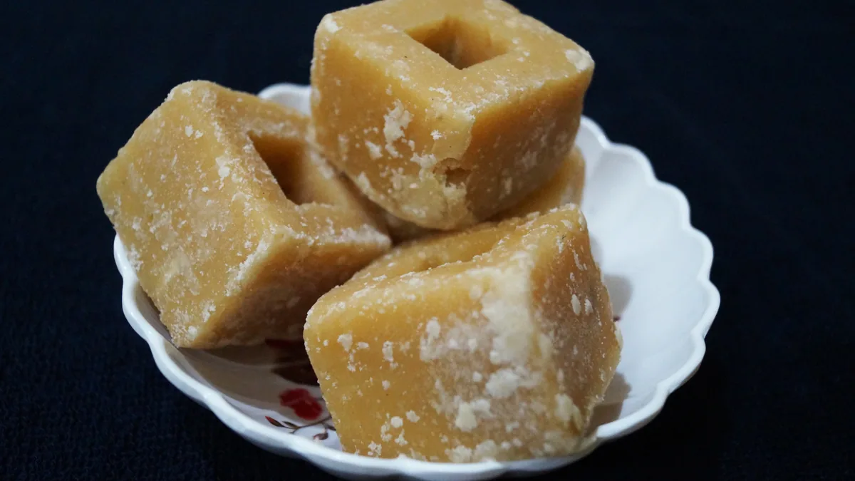 Unrefined golden-brown jaggery gur cubes served on a decorative plate