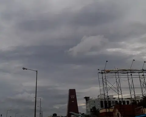 Dark cyclonic storm clouds over RK Beach Road in Visakhapatnam, Andhra Pradesh, showing stripped metal billboard frames and coastal structures battered by severe Bay of Bengal winds.