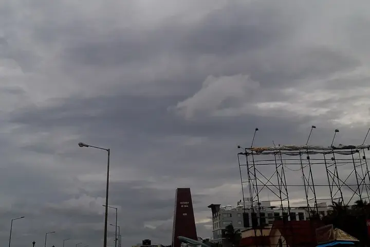 Dark cyclonic storm clouds over RK Beach Road in Visakhapatnam, Andhra Pradesh, showing stripped metal billboard frames and coastal structures battered by severe Bay of Bengal winds.