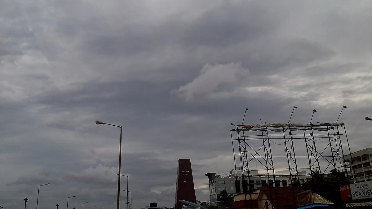 Dark cyclonic storm clouds over RK Beach Road in Visakhapatnam, Andhra Pradesh, showing stripped metal billboard frames and coastal structures battered by severe Bay of Bengal winds.