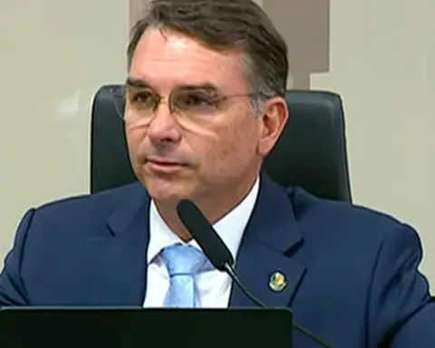 Brazilian Senator Flávio Bolsonaro wearing glasses, a dark navy suit, and a light blue tie seated behind a microphone at the Federal Senate in Brasília.