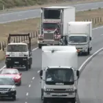 Passenger cars, SUVs, and heavy freight trucks driving along the curved multi-lane Hume Freeway at the Craigieburn Bypass in Victoria, Australia.