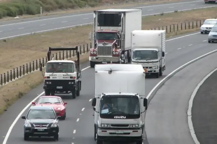 Passenger cars, SUVs, and heavy freight trucks driving along the curved multi-lane Hume Freeway at the Craigieburn Bypass in Victoria, Australia.