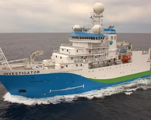 Port-side aerial view of the blue, white, and green CSIRO research vessel RV Investigator steaming through deep ocean waters off Tasmania.
