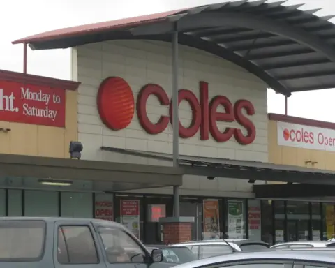 Exterior view of a Coles supermarket entrance at Kurralta Central in Australia with a curved roof awning and parked vehicles in the car park.
