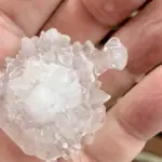 Close-up photograph of a person holding a large, spiky, translucent and white hailstone over a wooden deck in South-East Queensland.