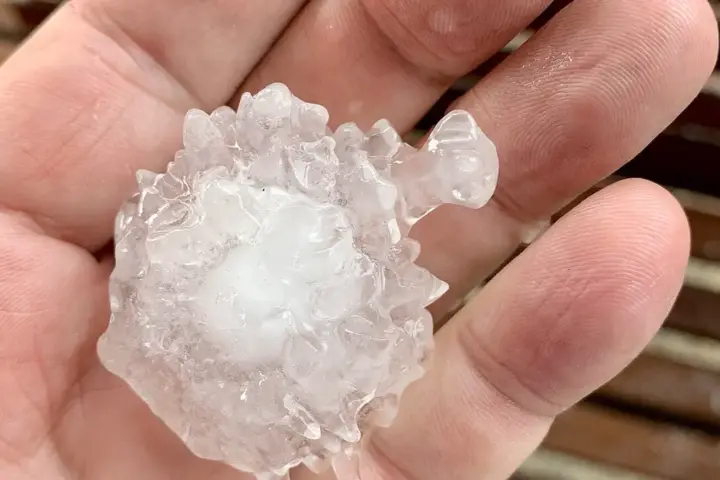 Close-up photograph of a person holding a large, spiky, translucent and white hailstone over a wooden deck in South-East Queensland.